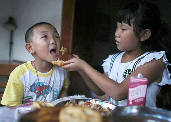 Guo's sister helps him eat supper while their parents are away from home. (Photo/China Daily)