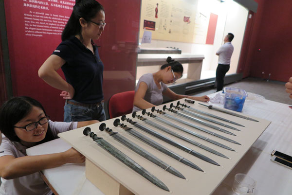Workers fasten bronze swords made more than 2,000 years ago on a panel. They will open to visitors in the Jinsha Site Museum in Chengdu, Sichuan province from August 20 to October 31. (Photo by Huang Zhiling/chinadaily.com.cn)
