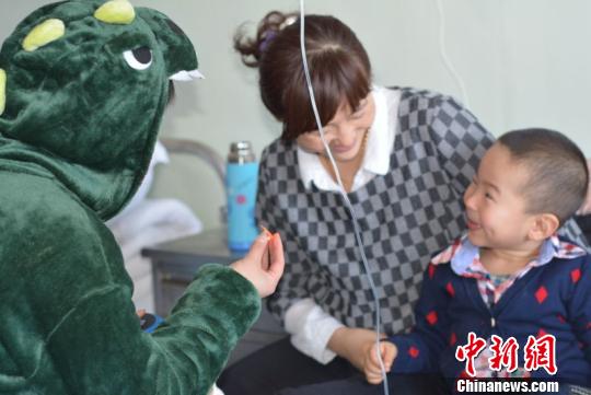 A volunteer dressed up as a dinosaur cheers up a boy. (Photo/chinanews.com)