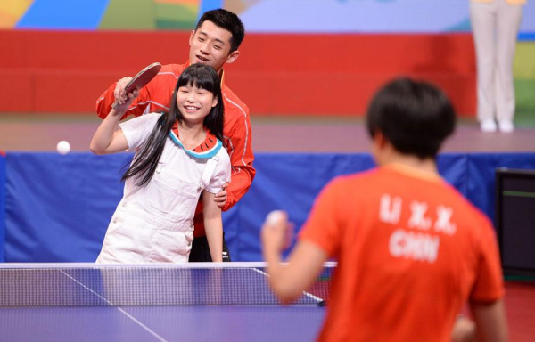 Zhang Jike, men's table tennis singles silver medalist in Rio Olympics, teaches a fan playing against Li Xiaoxia, a key member of Chinese women's team, at the Queen Elizabeth Stadium in Hong Kong, Aug 28, 2016. (Photo/Xinhua)