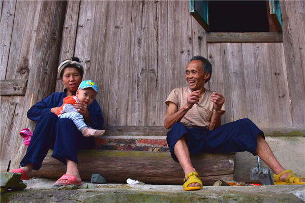 The grandparents take their grandson sitting at the gate of the house. (Photo by Zhang Xingjian/chinadaily.com.cn)