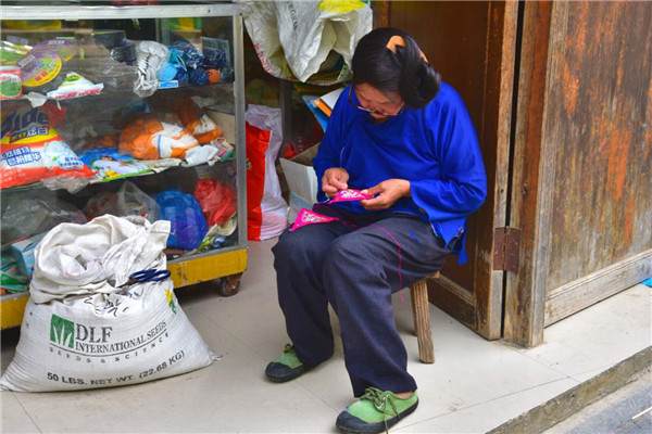 A senior local does the traditional sewing work at her shop. (Photo by Zhang Xingjian/chinadaily.com.cn)