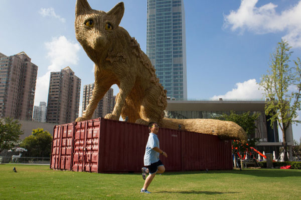 A child runs beside a straw fox during the 2016 Jing'an International Sculpture Expo at Jing'an Sculpture Park in Jing'an district, Shanghai, on Sept 20, 2016. The fox made by British artist Alex Rinsler has many manmade bird nests on its body. Cameras inside the nests record the lives of the birds living inside the nests. (Photo by Gao Erqiang/China Daily)