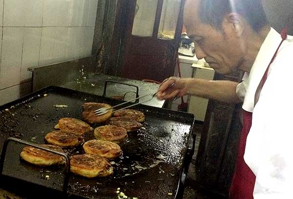Wu Gencheng prepares spring onion pancakes in his stall in Shanghai on Monday.(Yin Liqin/for China Daily)
