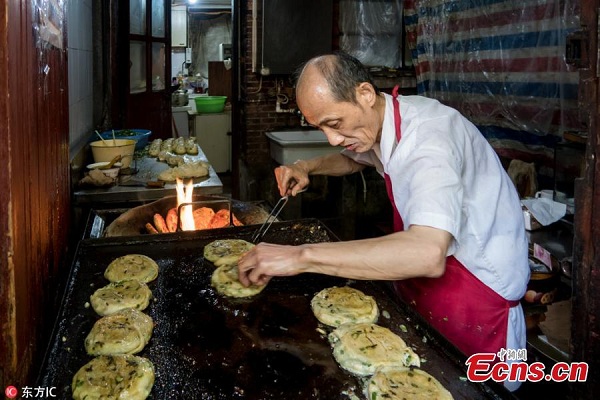 Wu Gencheng, more commonly known by his nickname A Da, makes scallion pancakes in his store in Shanghai, Sept. 22, 2016. (Photo/IC)