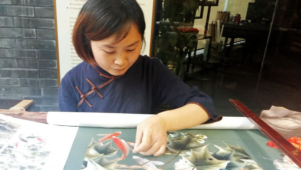 Jiang Mei shows off her skills of Shu embroidery with a piece featuring fish and flowers at the Chengdu Shu Brocade and Embroidery Museum. (Photo by Huang Zhiling/China Daily)