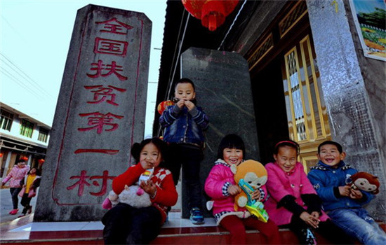 Children of Se ethnic group sit in front of a monument that reads China's No. 1 Poverty Relief Village at Chixi Village, Panxi town, Fuding city in East China's Fujian province, Feb 14. The village has shaken off poverty thanks to assistance from Party and government officials at all levels over the past 30 years. (Photo/Xinhua)