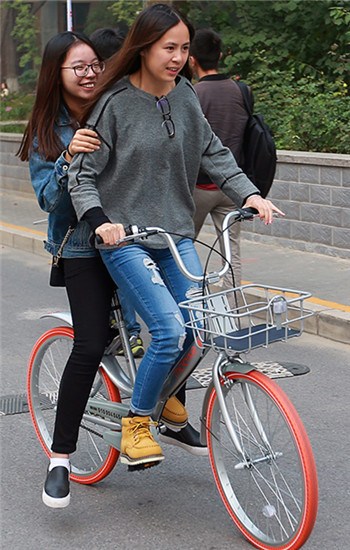 Reporters ride a Mobike in Beijing on Wednesday. (Photo by Zou Hong/China Daily)