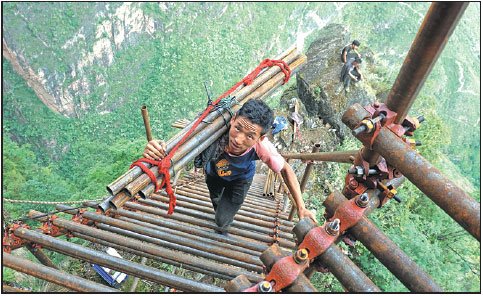 Mose Xiongti, 21, of Atuleer village, carries materials used in constructing a steel ladder that villagers soon will use to more safely traverse an 800-meter cliff to their homes. The village is in Liangshan Yi autonomous prefecture, Sichuan province.Provided To China Daily