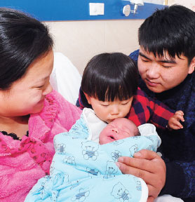 A girl kisses her little brother while their parents look on at a hospital in Fuyang, Anhui province. (Wang Biao / For China Daily)