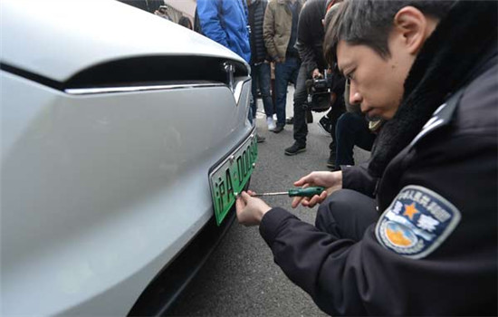 A traffic police officer from the Shanghai vehicle administration department installs the first special plate on a Tesla car in Shanghai, on Dec 1, 2016. (Photo by Gao Erqiang/chinadaily.com.cn)