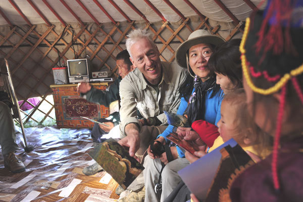 William Lindesay and his wife, Wu Qi, show Mongolian herders postcards of a more familiar Great Wall, near Beijing. James Lindesay / for China Daily