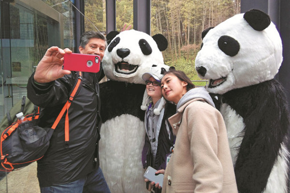 Madelyn Ruyle (middle), 11, from the United States, is one of 17 United Nations panda champions, 15 of whom are visiting Chengdu, Sichuan province, this week. Her father, who accompanied her, takes a photo. (Photo/China Daily)