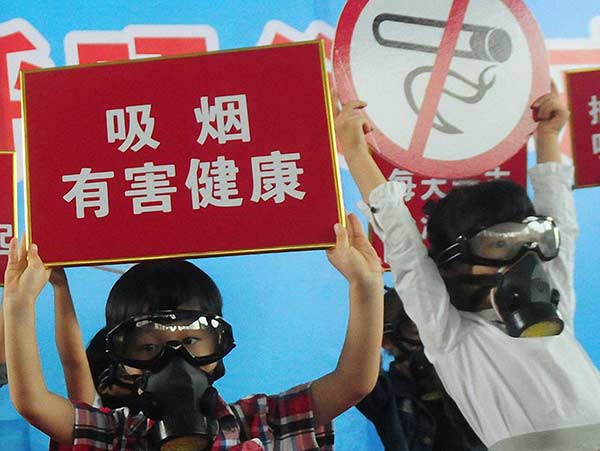 Children wearing gas masks hold anti-smoking signs to call on their parents to quit smoking at an event in Hangzhou on May 29, 2016.Lian Guoqing / For China Daily