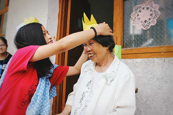 Tao Ruqin gives a paper crown to a senior resident at the leprosy recovery village in Zhuzhou, Hunan province. (Photo/China Daily)