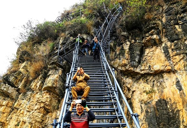 Tourists take photos while sitting on the steel ladder leading to Atuleer village in Sichuan province. (Wu Chuanming/For China Daily)