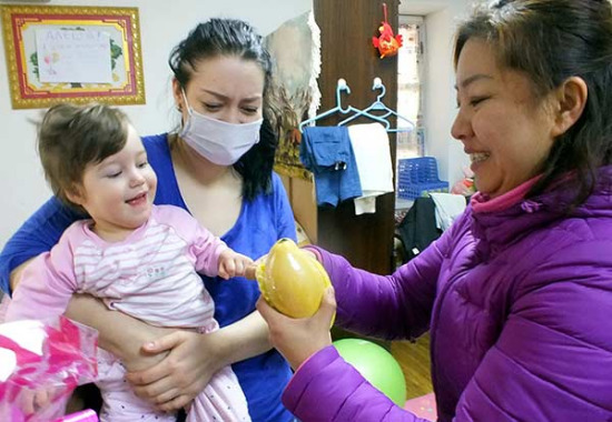Yang Tao, a local community worker, visits Elena Sibileva and her daughter Daria at their rented house in Harbin on Wednesday. The Russian single mother came to Harbin to seek treatment for her daughter, who has cerebral palsy. (Photo/CHINA DAILY)