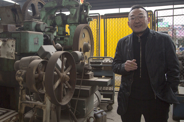 Tang Shigang poses with part of his collection of antique machine tools in Chongqing. (Photo provided to China Daily)