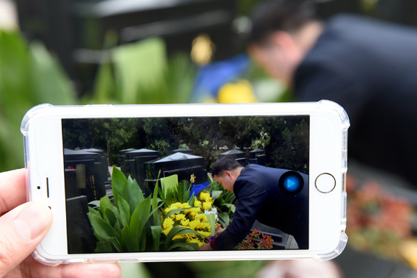 A worker from Yuhuatai Cemetery attends to a tomb while a colleague broadcasts the process live to a client in Nanjing, Jiangsu province, on Wednesday. (Photo/Xinhua)