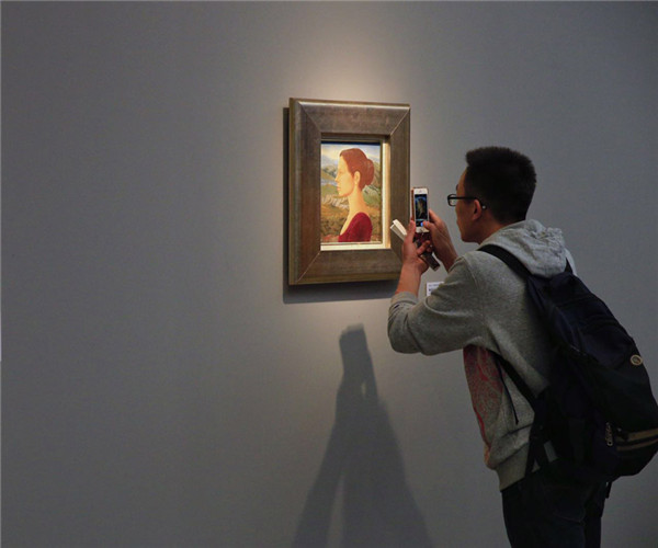 A visitor takes photos of a painting on display at the Voice of the Volga River exhibition at the National Art Museum of China in Beijing. (Photo by Jiang Dong/China Daily)