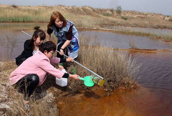 Staff members of the Dacheng county environmental protection bureau's monitoring station collect a water sample on Thursday from a polluted pit in Langfang, Hebei province.(Deng Jia/For China Daily