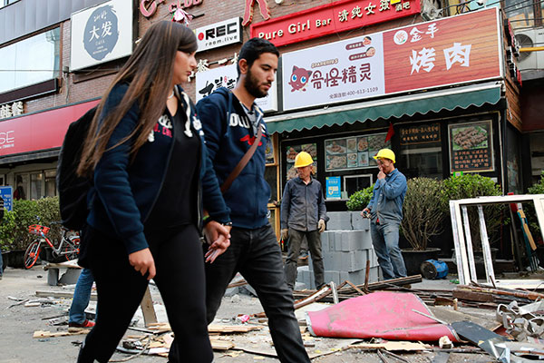 Two visitors walk along the Tonglihou Street in Beijing's Sanlitun area as urban management workers dismantle illegal buildings along the street on Monday.(Feng Yongbing/China Daily)