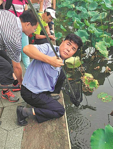 Hangzhou police officer Zhou Xiangjun helps a visitor in August to retrieve an item that had fallen into West Lake. (Photo provided to CHINA DAILY)