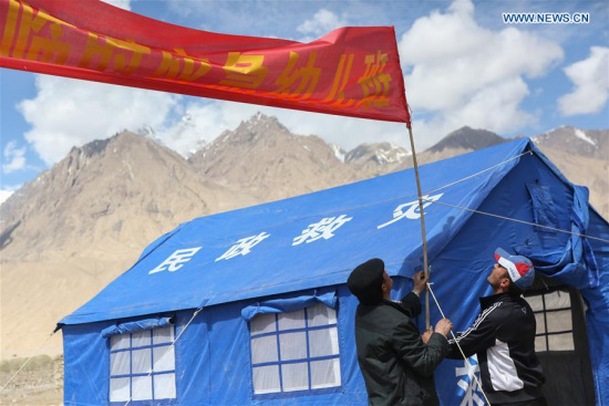 Rescuers set up a banner for a temporary kindergarten of an emergency shelter in Quzgun Village of quake-hit Taxkorgan County, northwest China's Xinjiang Uygur Autonomous Region, May 12, 2017. (Xinhua/Li Jing)