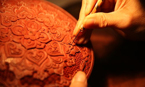 Designer carves on the round lacquer box. (Photo/Beijing Evening News)