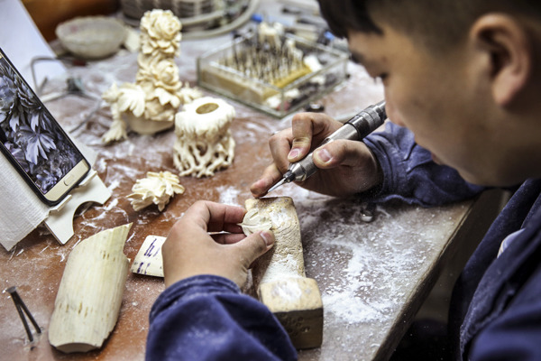Guo Chen carves a piece of ivory at his desk at the Beijing Ivory Carving Factory. (Photo by Zou Hong/China Daily)