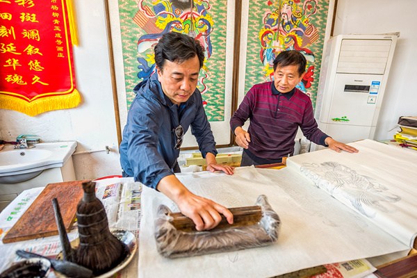 Huo Qingshun, an inheritor of the Yangliuqing New Year painting, teaches a visitor to use an ink mold to create a sketch of the traditional painting, April 28, 2017. (Photo by Liu Jie/provided to chinadaily.com.cn)
