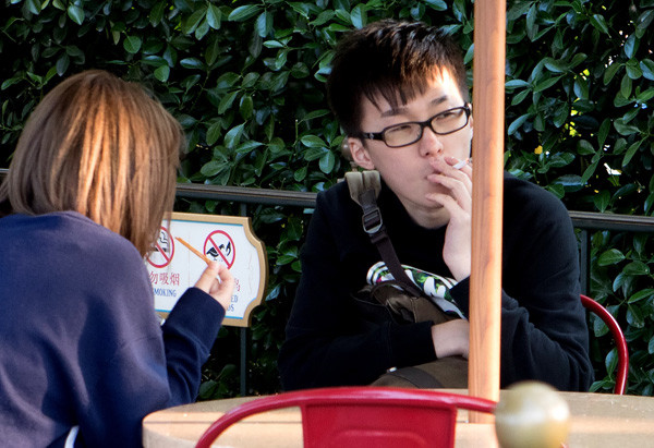 A tourist smokes beside a'No Smoking' sign at Shanghai Disneyland in April. (Photo by Gao Erqiang/China Daily)