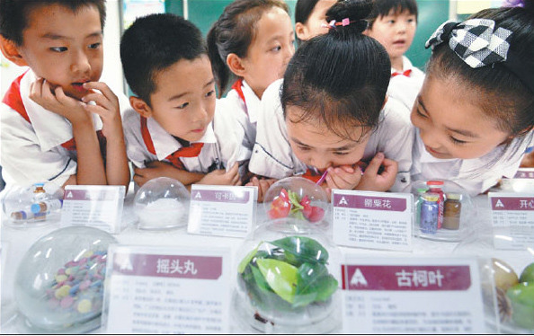 Students look at drugs displayed at a primary school in Handan, Hebei province, on Friday. The event, which was held by local police, aimed to help teach the children about the dangers of illegal substances. (Photo by Hao Qunying / For China Daily)