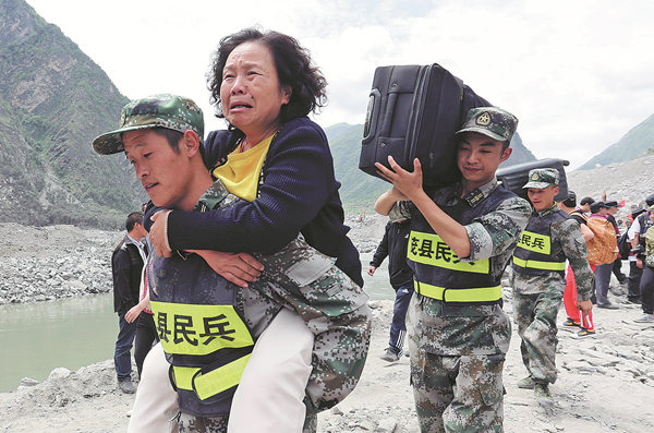 Reserve soldiers on Sunday carry victims and their belongings from Xinmo village on the road to safety. They were stuck on the mountain because of the landslide.