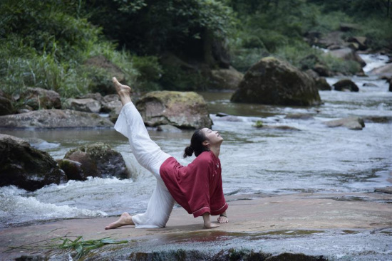 A woman practices yoga on the bank of a creek in Shuiwei Township in Xuyong County, southwest China's Sichuan Province, July 4, 2017. (Xinhua/Li Xin)