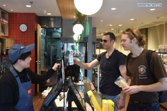 Tim Clancy (C), an Australian who has lived in Hangzhou for six years with his Chinese wife, takes his American friend to buy coffee and bread through mobile payment in Hangzhou, capital of east China's Zhejiang Province, April 14, 2017. (Xinhua/Huang Zongzhi)