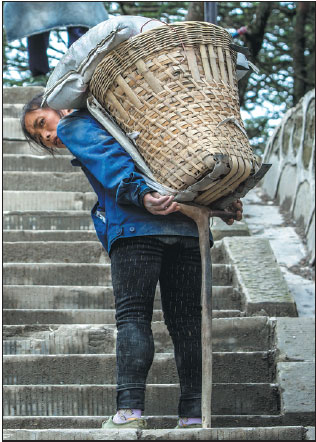 Deng uses a cane to prop up the load she is carrying while taking a short break on the mountain path.