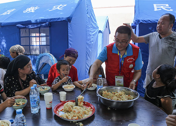 Residents eat pilafrice boiled in a seasoned liquid with meat and carrotsin a resettlement area for those displaced by the Jinghe earthquake in the Xinjiang Uygur autonomous region on Wednesday.(Photo/Xinhua)
