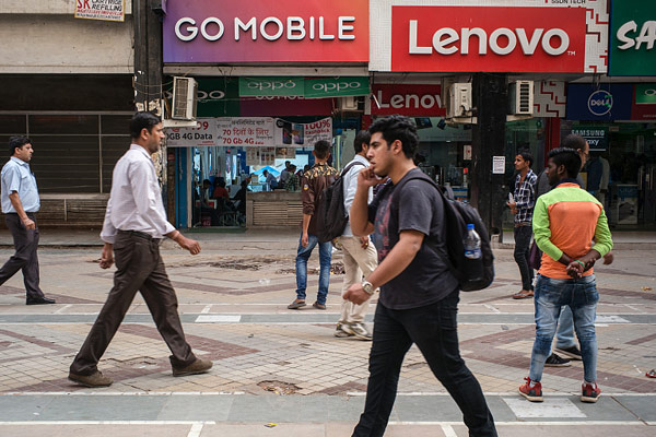 A pedestrian using a smartphone walks past stores selling mobile phones and accessories at the Nehru Place IT Market in New Delhi, India, May 30, 2017. (Photo/VCG)