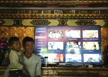Ciren Gesang, a resident in Zhaxi Tuomen community of Shannan Prefecture, China's Tibet Autonomous Region, stands in front of the internet television with his son in his hands. (Photo/China.org.cn)
