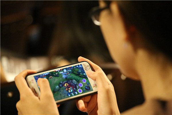 A woman plays the same game on her smartphone in a theater. (Photo by Li Sanxian, Yin Ming and Wang Gang/For China Daily)