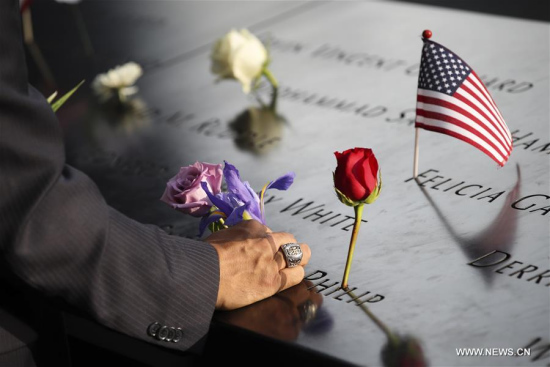 A man places a flower on a plate on which the names of 9/11 victims were inscribed around the South Pool at the National September 11 Memorial and Museum in New York, the United States, on Sept. 11, 2017. (Xinhua/Wang Ying)
