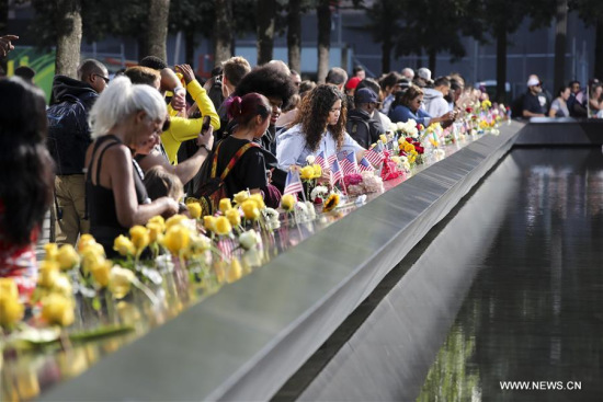 People place flowers on plates on which the names of 9/11 victims were inscribed around the South Pool at the National September 11 Memorial and Museum in New York, the United States, on Sept. 11, 2017. (Xinhua/Wang Ying)