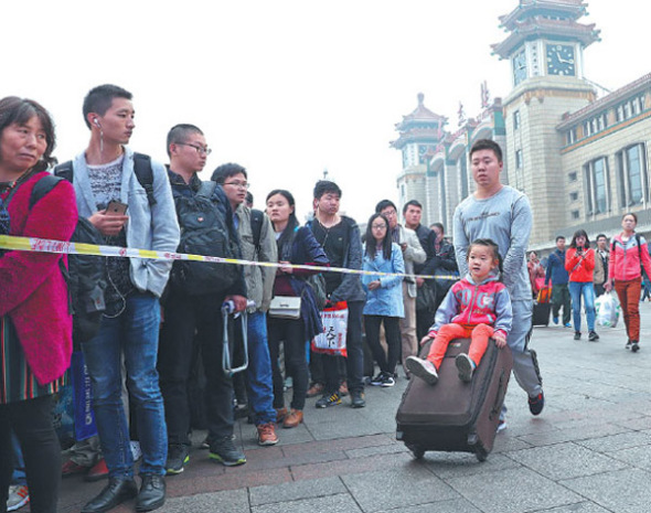 People wait in line for security checks outside the subway entrance at Beijing Railway Station on Sunday.(Photo by Zou Hong/China Daily)