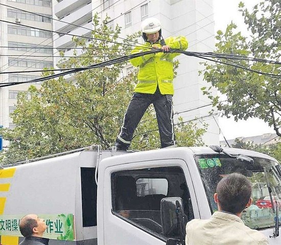 Police officer Yang Zhiguang climbs on a sanitation truck to make safe a loose cable at Pudongs Dezhou and Lingyan crossroads. (Ti Gong)
