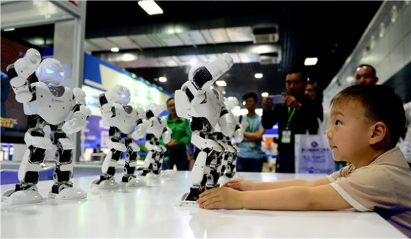 A boy plays with dancing robots at an intelligent devices exhibition in Luoyang, Henan province, in May. Photo/Xinhua