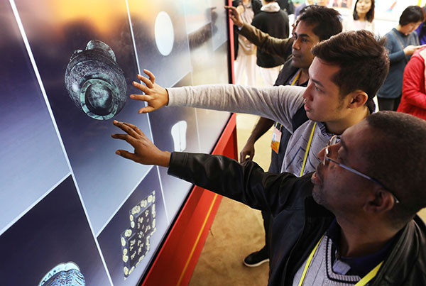 Zaw Ye Aung (center), a journalist from Skynet Up to Date media in Myanmar, and other reporters touch a screen to learn about a cultural relic at the digital Palace Museum section of an exhibition showcasing China's progress in the past five years. ZHU XINGXIN/CHINA DAILY