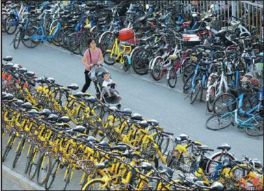 A woman pushes her child along the road between lines of bikes blocking a sidewalk in Beijing. (Zhu Xingxin / China Daily)