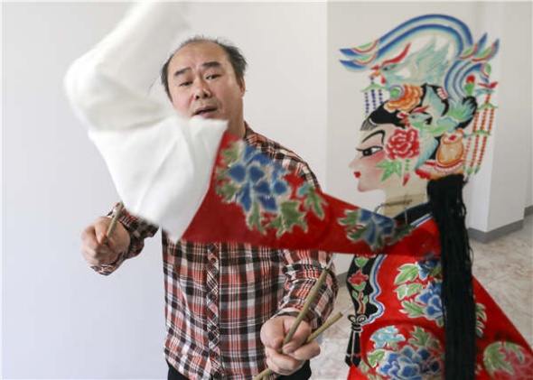 Lu Baogang, director of the Beijing Shadow Show Troupe, demonstrates how to manipulate a puppet in his office in Beijing. He believes reaching out to younger audiences may help revive the age-old art form. (Photo by Zou Hong/China Daily)
