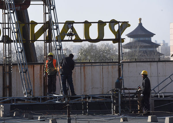 Construction workers remove a billboard from the roof of a building near Tiantan Park in Beijing on Nov 28. (Photo/Xinhua)